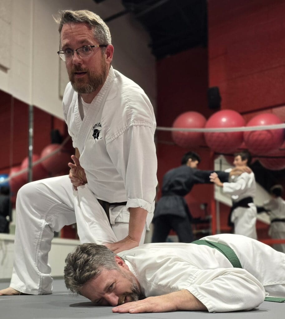 An adult karate student pinning another student on the floor.