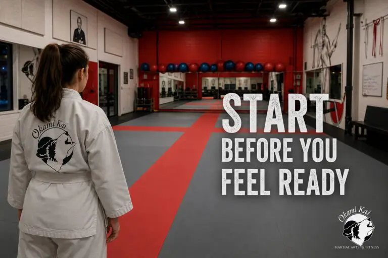 Woman in a white gi facing the Okami Kai dojo mats beneath the words &ldquo;Start Before You Feel Ready.&rdquo;